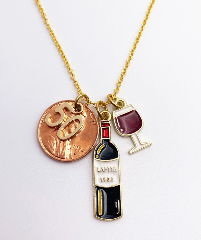 May include: Gold necklace with a 1982 penny charm with the number 50 on it, a wine bottle charm with the text "LAFFITE 1982" and a wine glass charm.