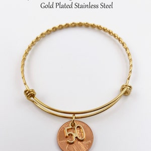 May include: Gold-plated expandable bangle bracelet with a charm featuring a penny with the number 50 on it. The bracelet is 60-62mm in size.