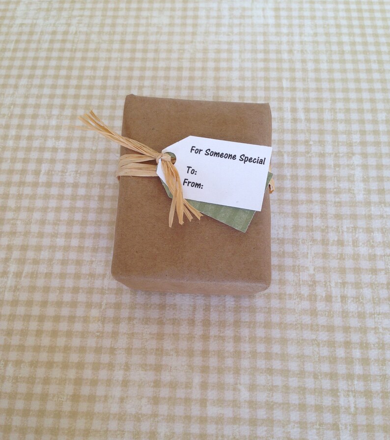 May include: A wrapped gift in brown paper, tied with raffia. A white tag with the text "For Someone Special" is attached, with spaces for "To:" and "From:" on a green paper backing. The gift is on a checkered beige surface.