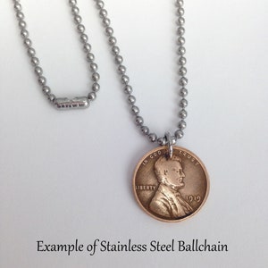 May include: A silver ball chain necklace with a 1919 penny pendant. The penny has the words "In God We Trust" and "Liberty" on it. The pendant is attached to the chain with a silver jump ring. Example of Stainless Steel Ballchain.