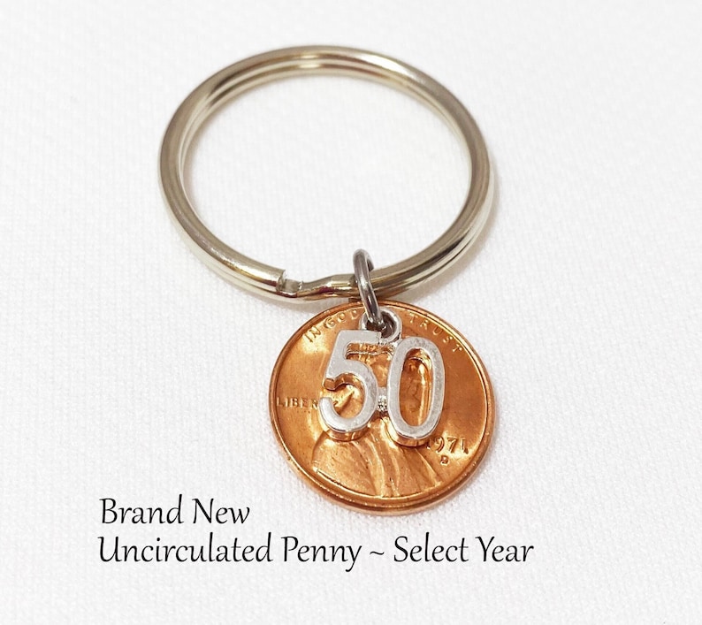 May include: A keychain featuring a copper penny with a silver '50' charm attached. The penny is from 1971. The text "Brand New Uncirculated Penny ~ Select Year" is visible below the penny.