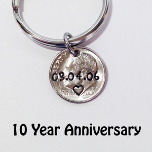 May include: A silver dime keychain with the date 03.04.06 stamped on it, along with a heart symbol. The keychain is attached to a silver ring. The text "10 Year Anniversary" is below the keychain.