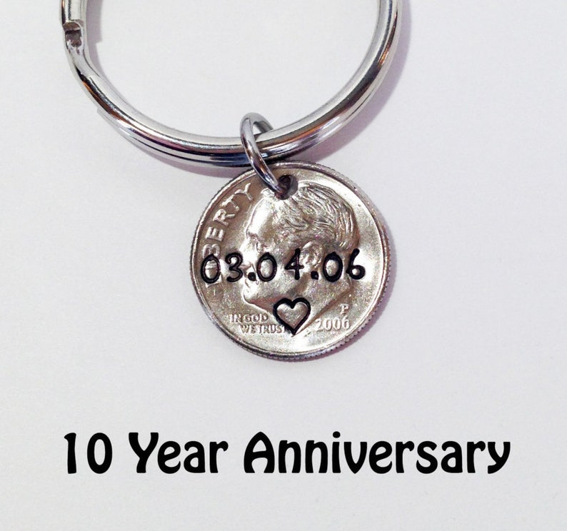 May include: A silver dime keychain with the date 03.04.06 stamped on it, along with a heart symbol. The keychain is attached to a silver ring. The text "10 Year Anniversary" is below the keychain.
