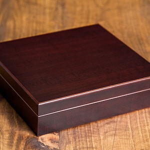 May include: A dark brown wooden box with a smooth, polished finish. The box has a hinged lid and a decorative inlay around the edge.