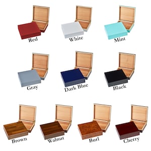 May include: Twelve wooden cigar boxes in a variety of colours. The boxes are open to reveal the natural wood interior. The colours are red, white, mint, grey, dark blue, black, brown, walnut, burl, and cherry.