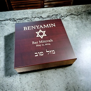 May include: A dark red wooden box with a gold Star of David and the text "BENYAMIN Bar Mitzvah May 11, 2024" and Hebrew text.
