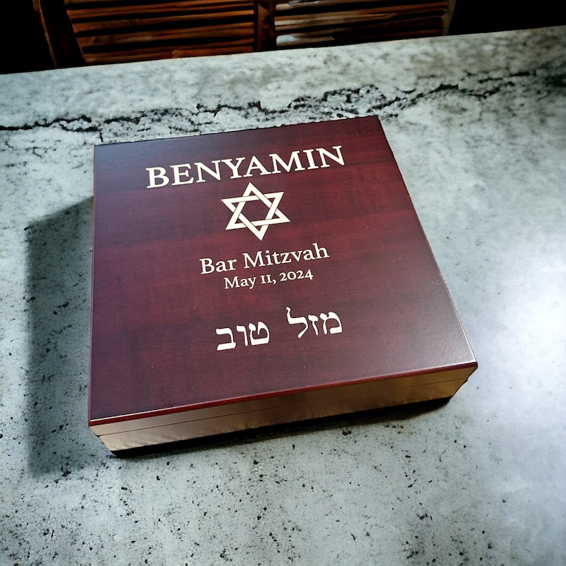 May include: A dark red wooden box with a gold Star of David and the text "BENYAMIN Bar Mitzvah May 11, 2024" and Hebrew text.