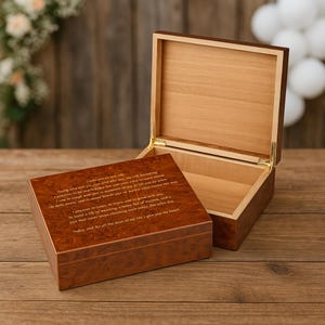 May include: A wooden keepsake box with a hinged lid, open to reveal the interior. The box is a warm brown color with a patterned finish. The lid of the box has an engraved message. The box is sitting on a wooden surface.