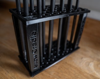 Könnte beinhalten: Ein schwarzer, 3D-gedruckter Pfeilhalter, der zur Aufnahme mehrerer Pfeile dient. Der Halter hat eine rechteckige Form mit vertikalen Stützen und einer perforierten Ober- und Unterseite. Der Text "Arrow Cradle" ist auf der Seite sichtbar. Die Pfeile sind schwarz.