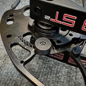 May include: Close-up of a black compound bow with red lettering. The bow features a series of adjustment settings and a black stabilizer. The bowstring and cables are visible, along with a black grip.