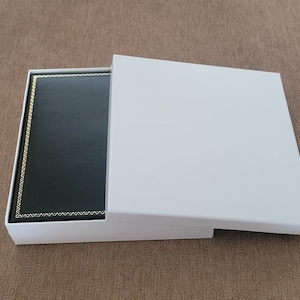 May include: A white box with a black interior. The box is open and the lid is propped up. The interior of the box is lined with black fabric.