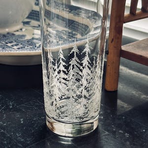 May include: A clear glass tumbler with a textured surface and a white tree design. The glass is cylindrical and has a thick base. The tree design is etched into the glass, creating a frosted effect.
