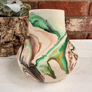 May include: A decorative ceramic vase with a unique marbled design. The vase features a cream-colored base with swirling patterns of green, brown, and black. The vase has a rounded body and a slightly flared opening, perfect for displaying flowers or as a standalone art piece.