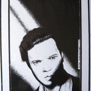 以下が含まれることがあります： 男性の顔の白黒インク画。真剣な表情をしている。点描画で描かれており、質感のある効果を生み出している。男性の髪は短く、横に梳かされている。絵は黒い額縁に入っている。