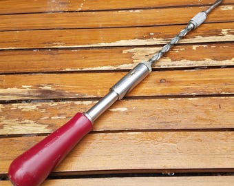 May include: A vintage Yankee spiral ratchet screwdriver with a red wooden handle and a silver metal shaft. The drill bit is visible at the end. The tool is lying on a wooden surface.
