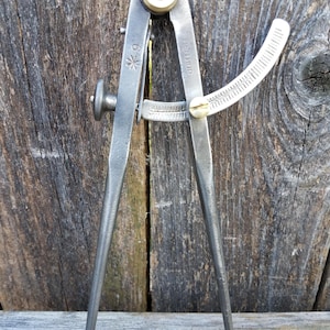 May include: A metal drafting compass with two pointed legs, a brass adjustment knob at the top, and a curved scale marked with 6 inches. The tool features the text BEN HUR and a star symbol stamped into the metal frame for precise measurements.