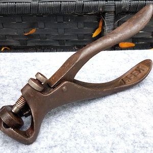 May include: A vintage brown metal saw set tool with a lever-action handle and an adjustable screw mechanism. The word APEX is embossed on the handle, and the tool features a circular rotating head with numbered settings for precision adjustment.