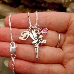 May include: A silver chain necklace with a silver fairy charm and a pink crystal. The charm has a letter 'D' attached to it.