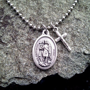 Puede incluir: Collar de cadena de plata con un colgante ovalado de plata que representa a San Expedito y el texto "St. Expeditus" e "Italia". Un dije de cruz de plata cuelga de la cadena.