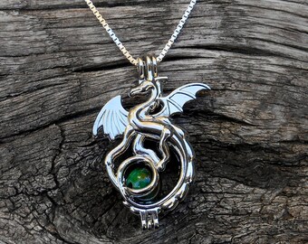 May include: Silver dragon charm necklace with a green gemstone in the center. The dragon is curled around the stone, with its wings spread out.