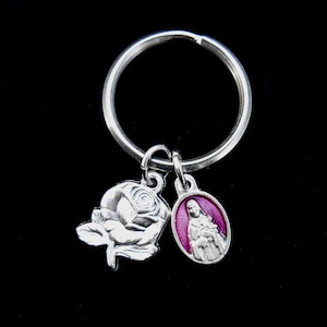 May include: Silver keychain with a rose charm and a charm featuring a religious figure in a pink robe.