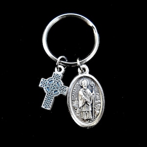 May include: Silver keychain with a Celtic cross and a Saint Patrick medal. The medal features a depiction of Saint Patrick holding a staff and a shamrock.