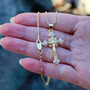 May include: A gold chain necklace with a gold and clear crystal Jesus crucifix pendant.