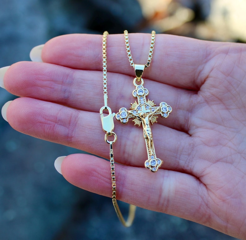 May include: A gold chain necklace with a gold and clear crystal Jesus crucifix pendant.