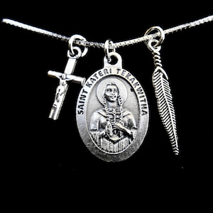 May include: Silver necklace with three charms: a cross, a medal of Saint Kateri Tekakwitha, and a feather.