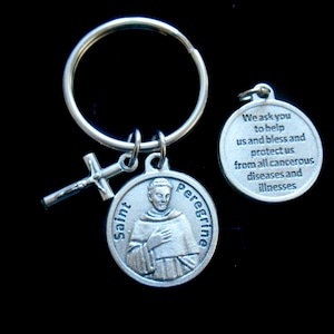 May include: Silver keychain with a round charm featuring a depiction of Saint Peregrine, a cross, and a round charm with the text "We ask you to help us and bless and protect us from all cancerous diseases and illnesses".
