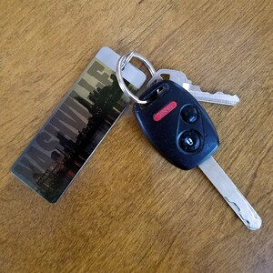 May include: A black car key with a silver key ring attached to a keychain with the word "Asheville" printed on it.