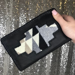 May include: Black leather wallet with a geometric patterned flap. The flap is made of a white, gray, and black fabric.