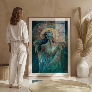 May include: A framed art print depicting a teal and gold illustration of a woman with closed eyes and outstretched arms. The artwork features a gold halo and flowing teal and gold garments. The print is in a light wood frame.