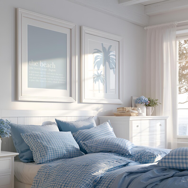 May include: A bedroom scene with a white bed frame, blue and white checkered bedding, and several pillows. Two framed prints hang above the bed, one with text that reads "the beach" and the other with palm tree silhouettes. A white dresser and window with sheer curtains are also visible.