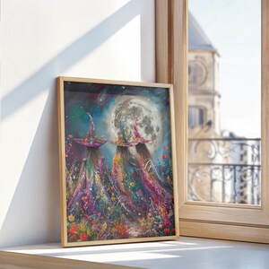 May include: Two witches wearing colorful hats and dresses walk through a field of flowers under a full moon. The painting is framed in a light wood frame.