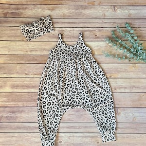 May include: A white and black leopard print romper with matching headband. The romper has a scoop neckline and a relaxed fit. The headband is a knotted style. The outfit is made of a soft, lightweight fabric.