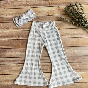 May include: A matching set of baby or toddler clothing, featuring a pair of flared pants and a headband. Both items are patterned with a gray and white gingham check design. The pants have a high waistband.