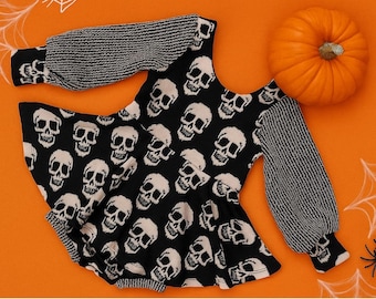 May include: A black and white skull-print top with long sleeves, a peplum hem, and striped sleeves. An orange pumpkin, spider, and spiderwebs are on an orange background. Halloween-themed clothing.
