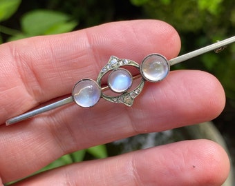 Op de afbeelding: Een zilveren broche met drie maansteen-cabochons en een diamant accent. De broche heeft de vorm van een gestileerd oog.