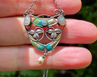 May include: A silver pendant necklace with a green, blue and gold enamel design. The pendant features a floral motif with three pearl accents. The necklace is on a silver chain.