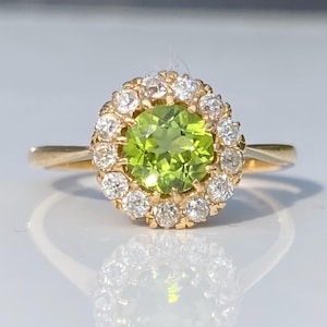 May include: A gold ring with a central, bright green gemstone, surrounded by a halo of white diamonds. The ring has a plain gold band, and the setting highlights the gemstones. This ring is a classic piece of jewellery, suitable for special events.