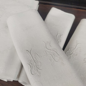 May include: White linen napkins with embroidered floral patterns. The napkins are folded, displaying the delicate embroidery. The overall aesthetic is classic and elegant, suitable for formal dining or special occasions.