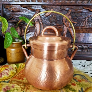 Peut inclure: Une casserole en cuivre avec une finition martelée et une poignée en laiton. La casserole a un couvercle et est posée sur un tissu à motifs floraux.