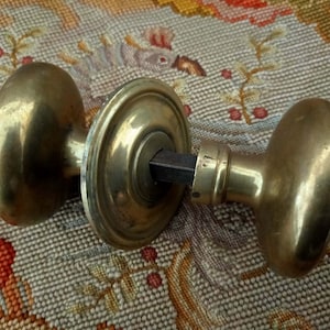 May include: A pair of antique brass door knobs with a round, slightly domed shape. The knobs are connected by a metal rod.