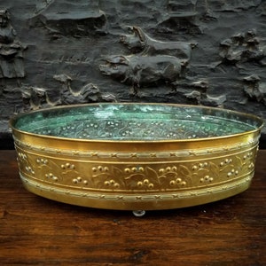 Peut inclure: Un pot rond en métal doré avec un motif floral décoratif. Le pot a un fond miroir et repose sur une surface en bois.
