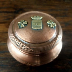 May include: A copper trinket box with a hinged lid. The lid is decorated with a gold crest, a crown, and three shamrocks.