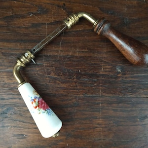 Peut inclure: Une poignée de porte ancienne avec une poignée en céramique blanche ornée d'un motif floral rouge, bleu et jaune. La poignée présente des accents en laiton et une poignée en bois foncé. Sur une surface en bois foncé.