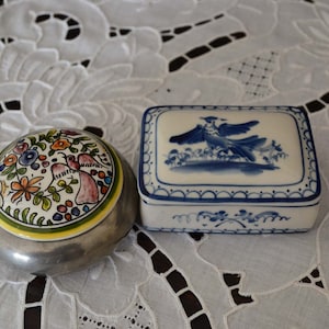 Peut inclure: Deux boîtes décoratives avec des motifs floraux et d'oiseaux. La boîte de gauche est en argent avec un motif floral coloré. La boîte de droite est blanche avec un motif d'oiseau bleu.