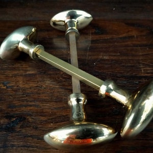 May include: Three antique brass door knobs with oval-shaped plates and a decorative design. The knobs are arranged in a triangular pattern on a wooden surface.