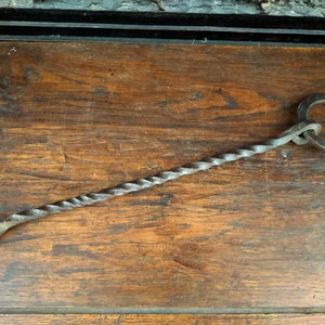 May include: A twisted metal fireplace tool with a ring at the end. The tool is made of dark metal and has a rustic look.